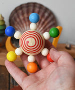 Mader carousel wooden baby grapsing toy with rainbow beads in an adult's hand.
