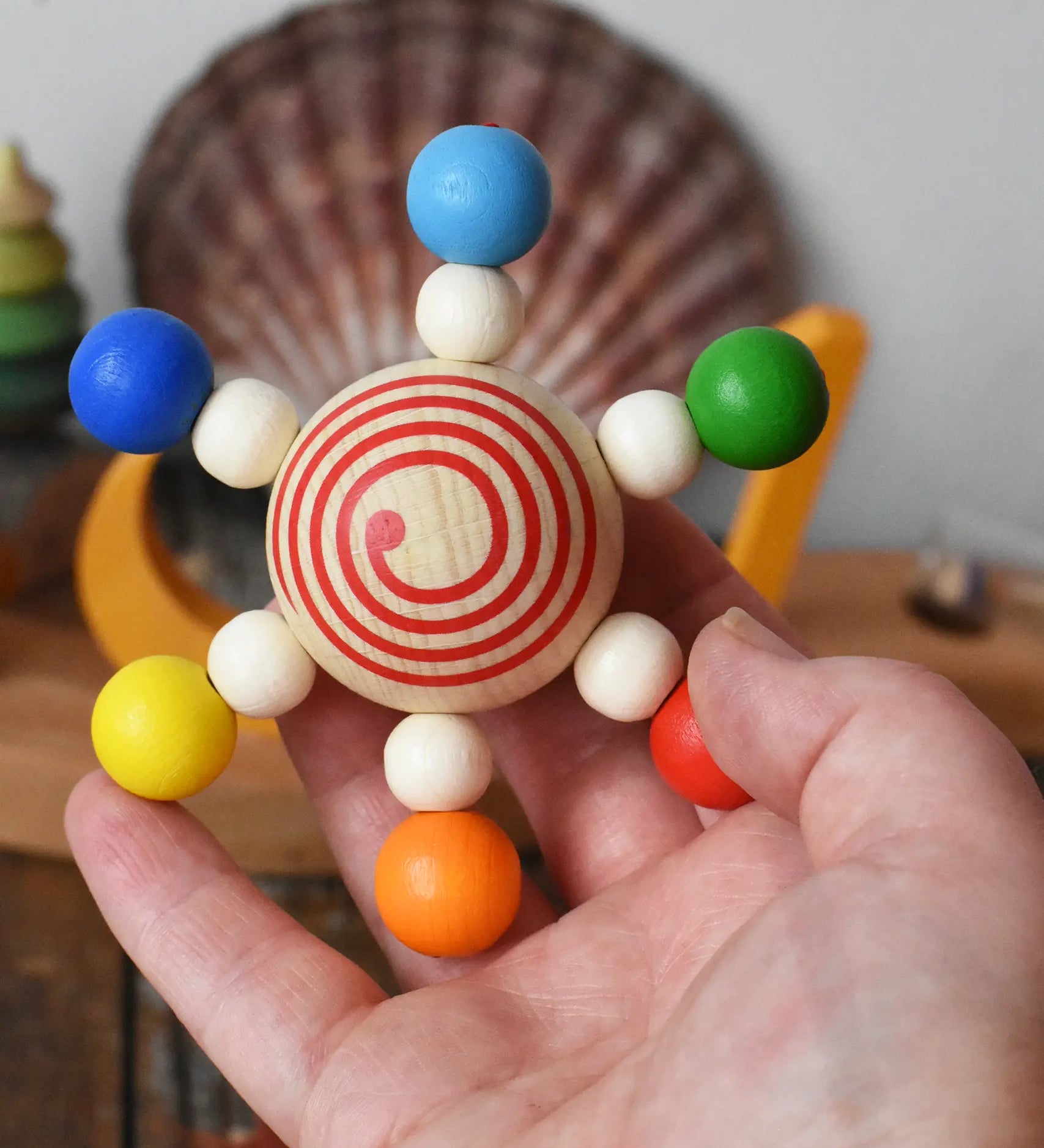 Mader carousel wooden baby grapsing toy with rainbow beads in an adult's hand.