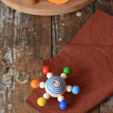 Mader carousel wooden baby grapsing toy with rainbow beads placed on a wooden surface. 