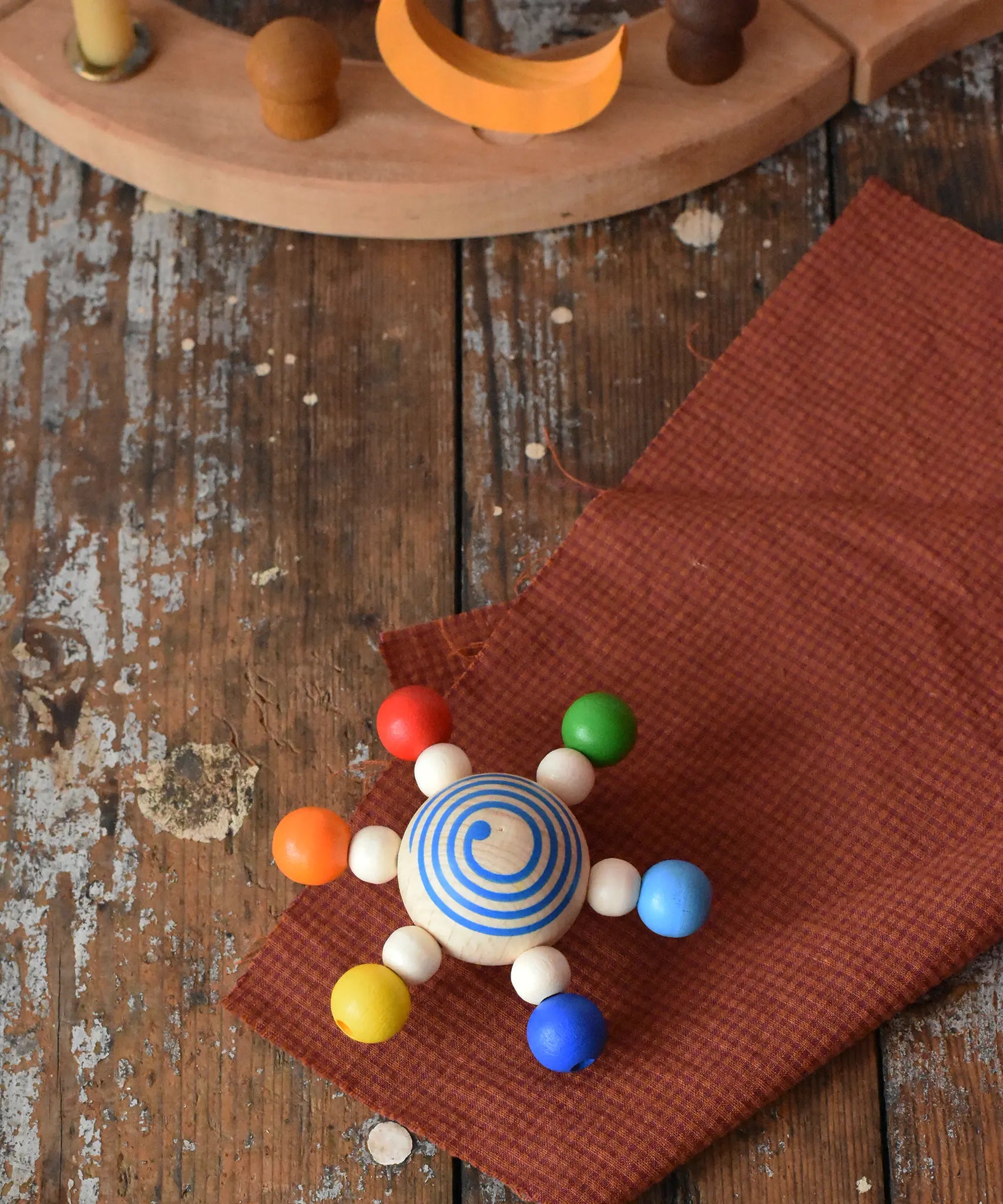 Mader carousel wooden baby grapsing toy with rainbow beads placed on a wooden surface. 