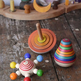 Mader carousel wooden baby grapsing toy with rainbow beads, orange first spinning top and striped roly poly pear toy placed on a wooden surface in front of a decorated Grimm's celebration ring.