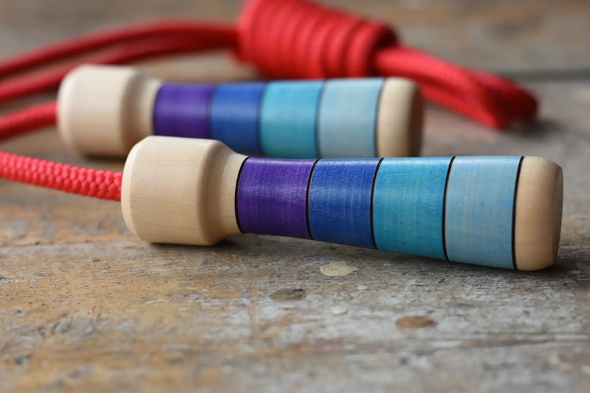 Mader Kreiselmanufaktur Children's Skipping Rope with Purple Handles placed on a wooden surface in the Babipur playroom. Close up of teh handles.