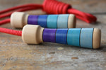Mader Kreiselmanufaktur Children's Skipping Rope with Purple Handles placed on a wooden surface in the Babipur playroom. Close up of teh handles.