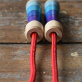 Close up of top of the handles on the Mader Kreiselmanufaktur Children's Skipping Rope with Purple Handles placed on a wooden surface in the Babipur playroom. 