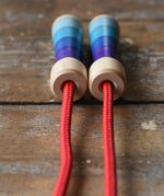 Close up of top of the handles on the Mader Kreiselmanufaktur Children's Skipping Rope with Purple Handles placed on a wooden surface in the Babipur playroom. 