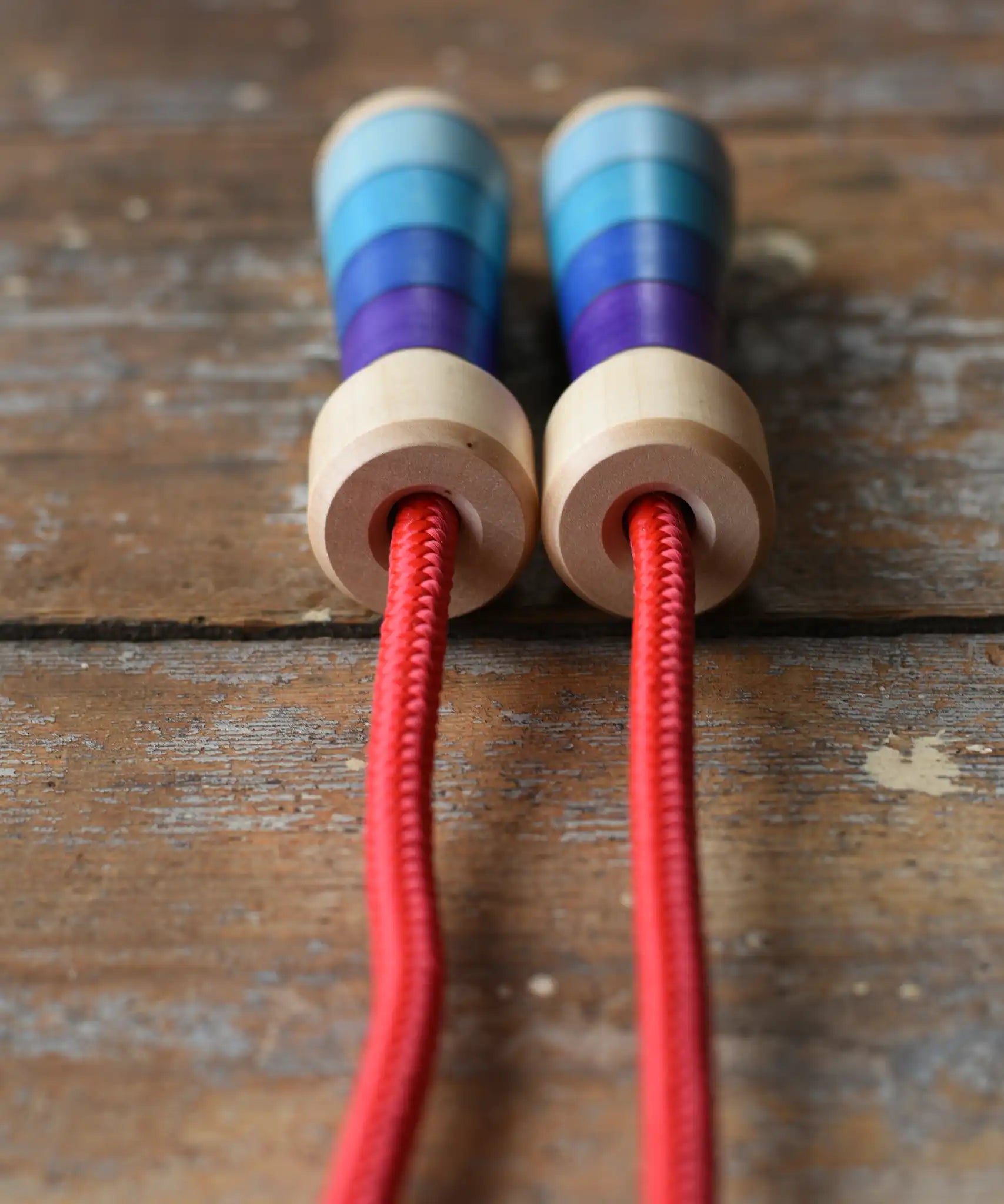 Close up of top of the handles on the Mader Kreiselmanufaktur Children's Skipping Rope with Purple Handles placed on a wooden surface in the Babipur playroom. 