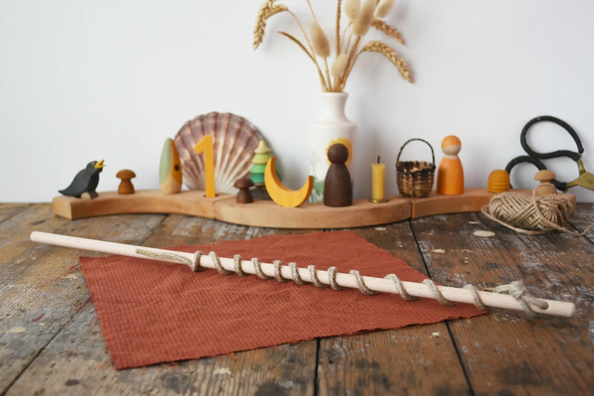 Stick from the Mader Kreiselmanufaktur Classic Whip Wooden Spinning Top placed on a wooden desk in the Babipur playroom. Decorated Grimm's celebration ring can be seen in the background. 