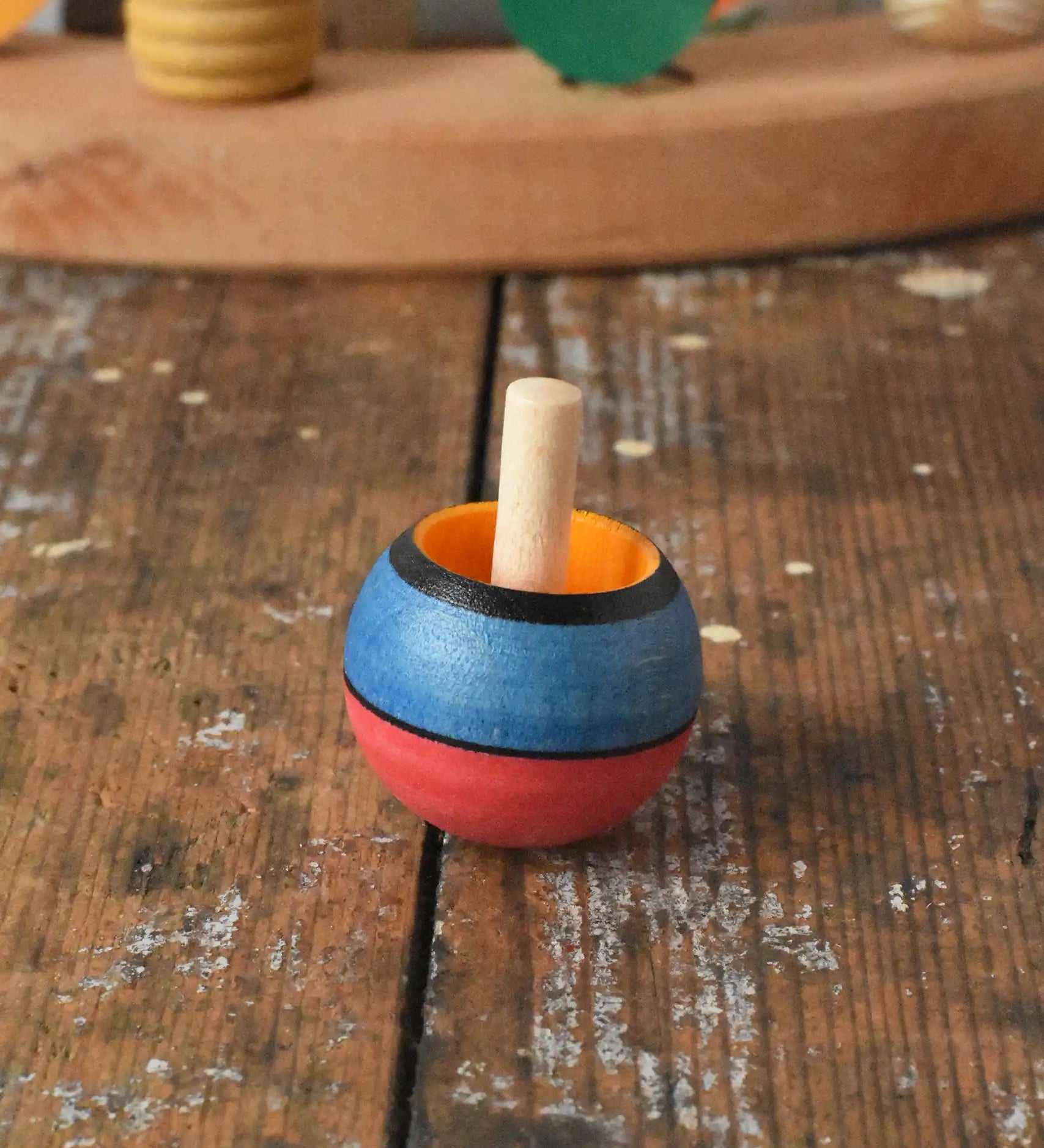 Mader Kreiselmanufaktur confetti turn-over wooden spinning top placed on a wooden desk in the Babipur playroom. 