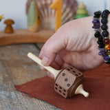 Mader Dice Spinning Top being placedon a wooden desk by an adult's hand in the Babipur playroom.