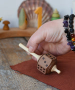 Mader Dice Spinning Top being placedon a wooden desk by an adult's hand in the Babipur playroom.