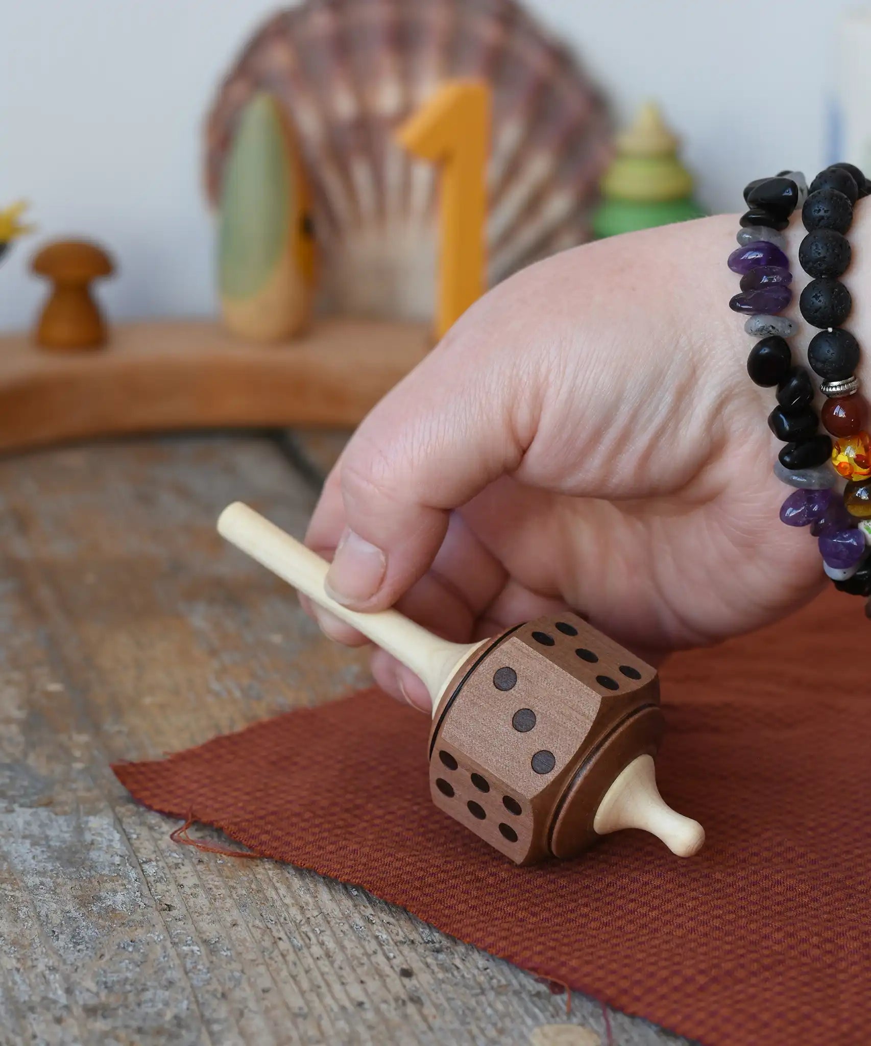 Mader Dice Spinning Top being placedon a wooden desk by an adult's hand in the Babipur playroom.