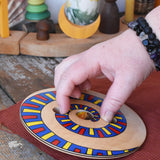 Mader Disc spinning Top Geometric placed on a wooden desk in the Babipur playroom. An adult hand ready to spin it.