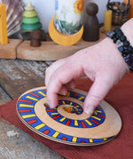 Mader Disc spinning Top Geometric placed on a wooden desk in the Babipur playroom. An adult hand ready to spin it.