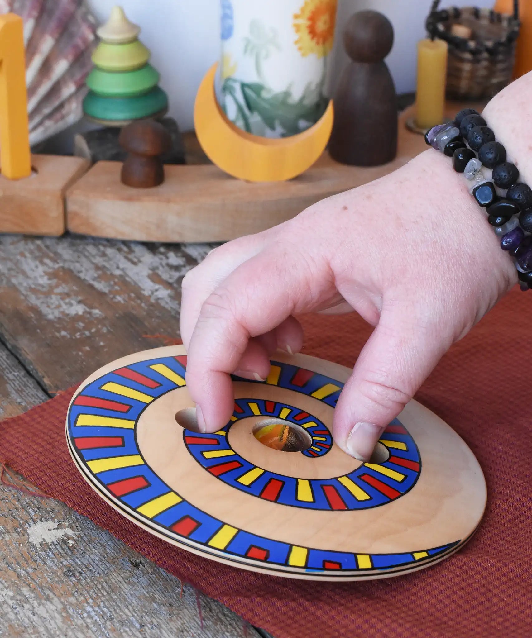 Mader Disc spinning Top Geometric placed on a wooden desk in the Babipur playroom. An adult hand ready to spin it.
