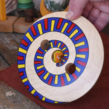 Mader Disc spinning Top Geometric placed on a wooden desk in the Babipur playroom. Adult hand holding it up 