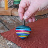 Mader dragon egg spinning top placed on apiece of cloth in the Babipur playroom. The toy is held upright by and adult's hand. 