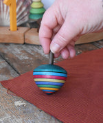 Mader dragon egg spinning top placed on apiece of cloth in the Babipur playroom. The toy is held upright by and adult's hand. 