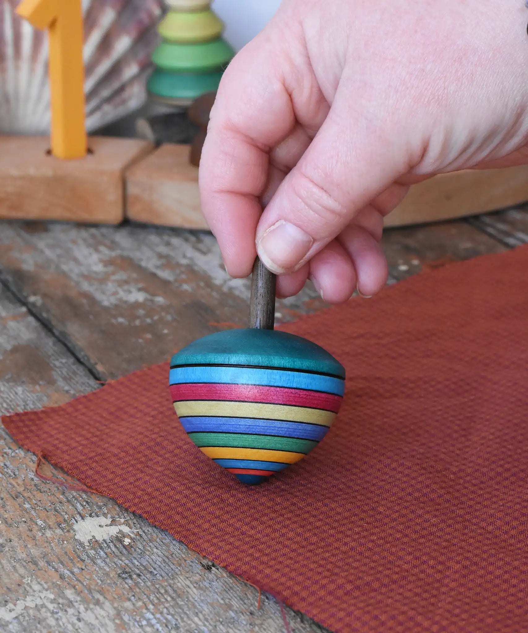 Mader dragon egg spinning top placed on apiece of cloth in the Babipur playroom. The toy is held upright by and adult's hand. 