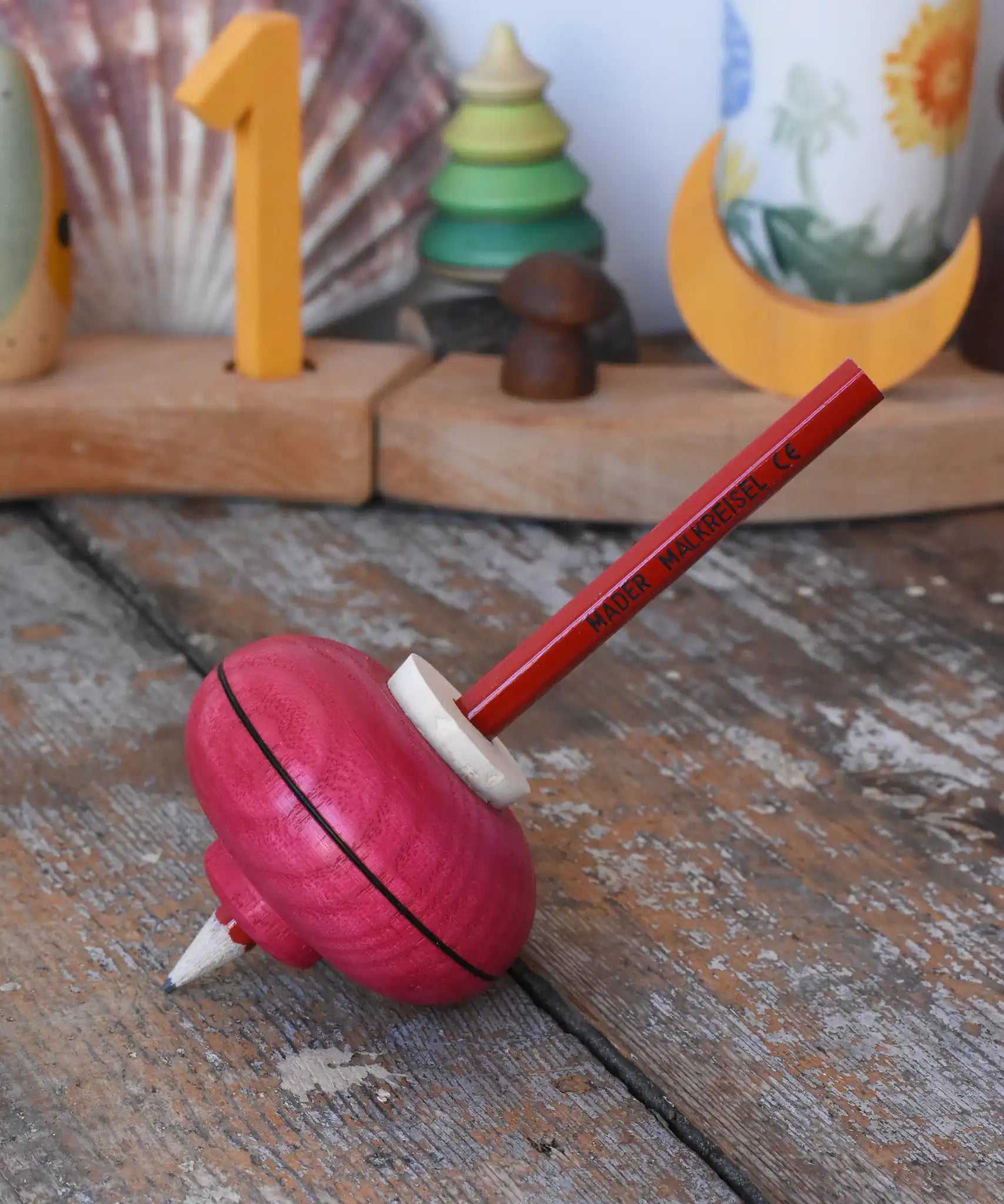 Mader Drawing spinning top in red placed on a wooden desk in the Babipur playroom.