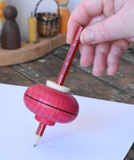 Mader Drawing spinning top in red placed on paper which has pencil marks on in the Babipur playroom.