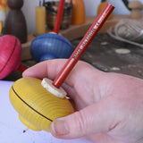 Mader Drawing spinning top in an adult hand. The wooden body has a cork centre with a wooden pencil slotted inside.