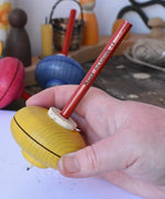 Mader Drawing spinning top in an adult hand. The wooden body has a cork centre with a wooden pencil slotted inside.