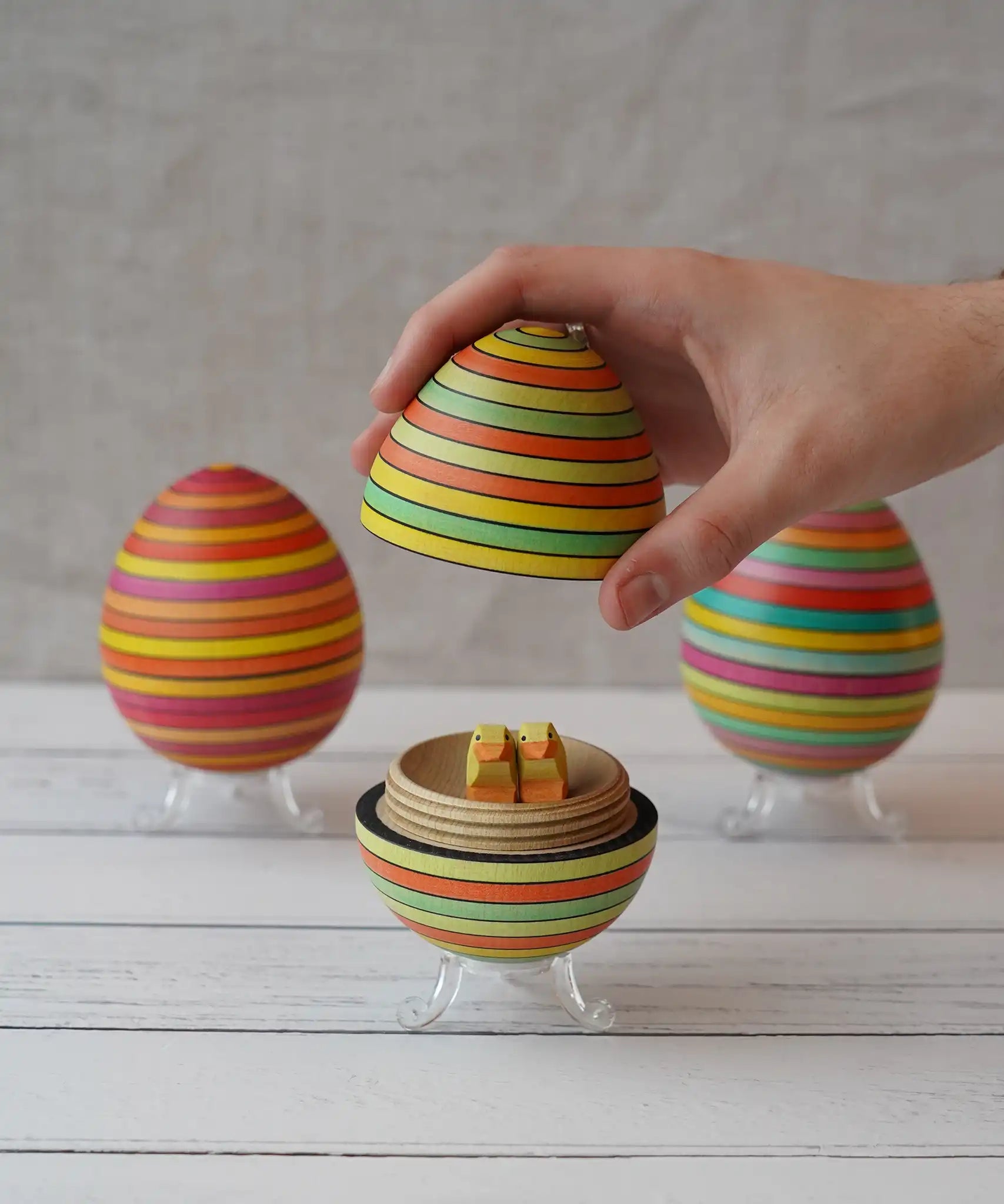Mader Summer stripe egg with two little Bumbu chicks placed inside, an adult hand can be seen lifting the lid off.
