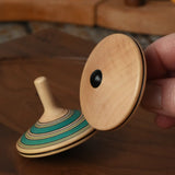 Bottom of the Mader Kreiselmanufaktur fado maple wooden finger spinning top in an adult's hand.