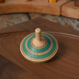 Green Mader Kreiselmanufaktur fado maple wooden finger spinning top placed on a walnut spinning plate in the Babipur playroom.