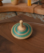 Green Mader Kreiselmanufaktur fado maple wooden finger spinning top placed on a walnut spinning plate in the Babipur playroom.