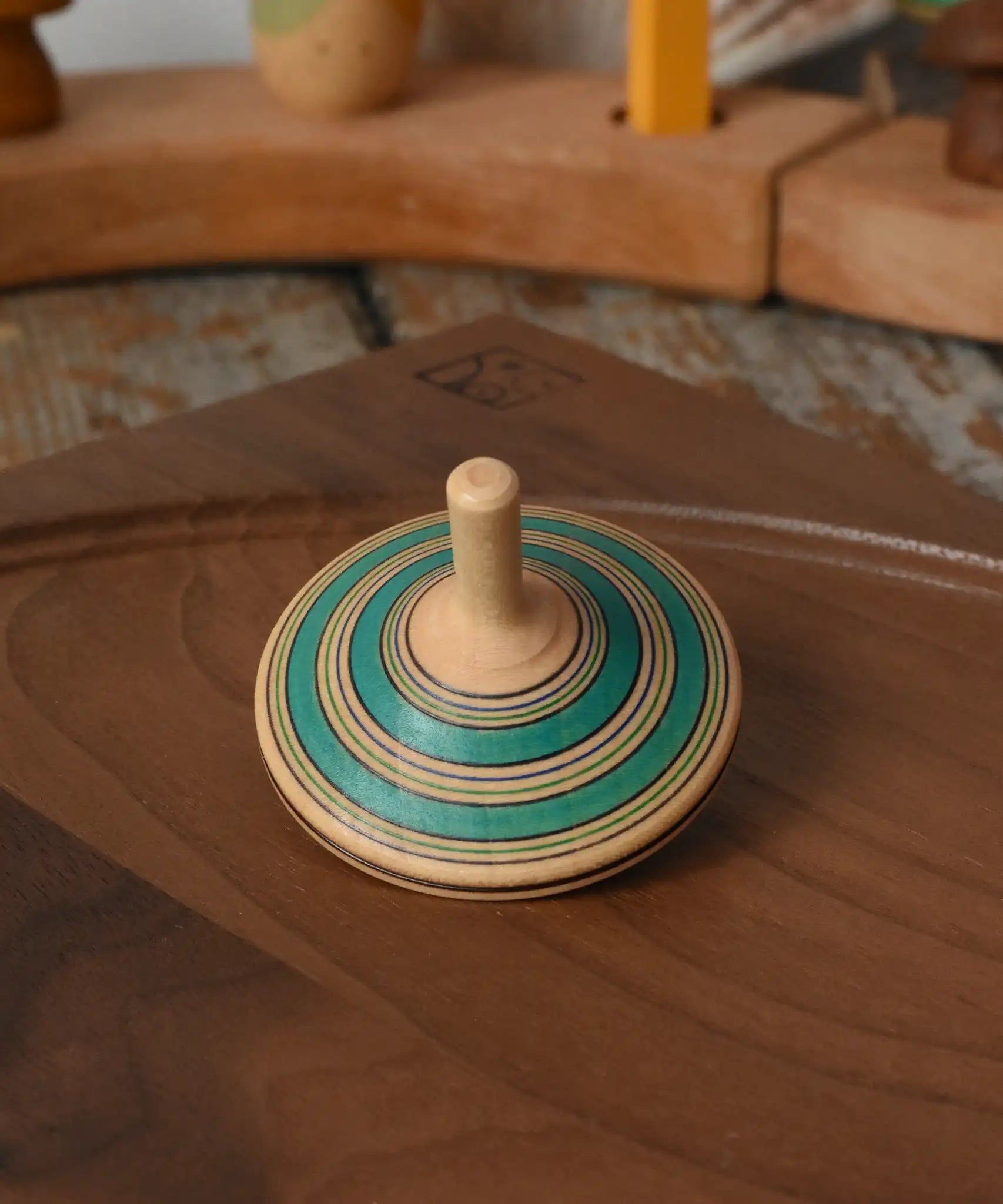 Green Mader Kreiselmanufaktur fado maple wooden finger spinning top placed on a walnut spinning plate in the Babipur playroom.