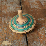 Green Blue Mader Kreiselmanufaktur fado maple wooden finger spinning top placed on a wooden surface in the Babipur playroom.