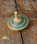 Green Blue Mader Kreiselmanufaktur fado maple wooden finger spinning top placed on a wooden surface in the Babipur playroom.