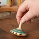 Mader Kreiselmanufaktur fado maple wooden finger spinning top being placed on a walnut spinning board by and adult hand in the Babipur playroom.