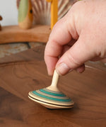 Mader Kreiselmanufaktur fado maple wooden finger spinning top being placed on a walnut spinning board by and adult hand in the Babipur playroom.