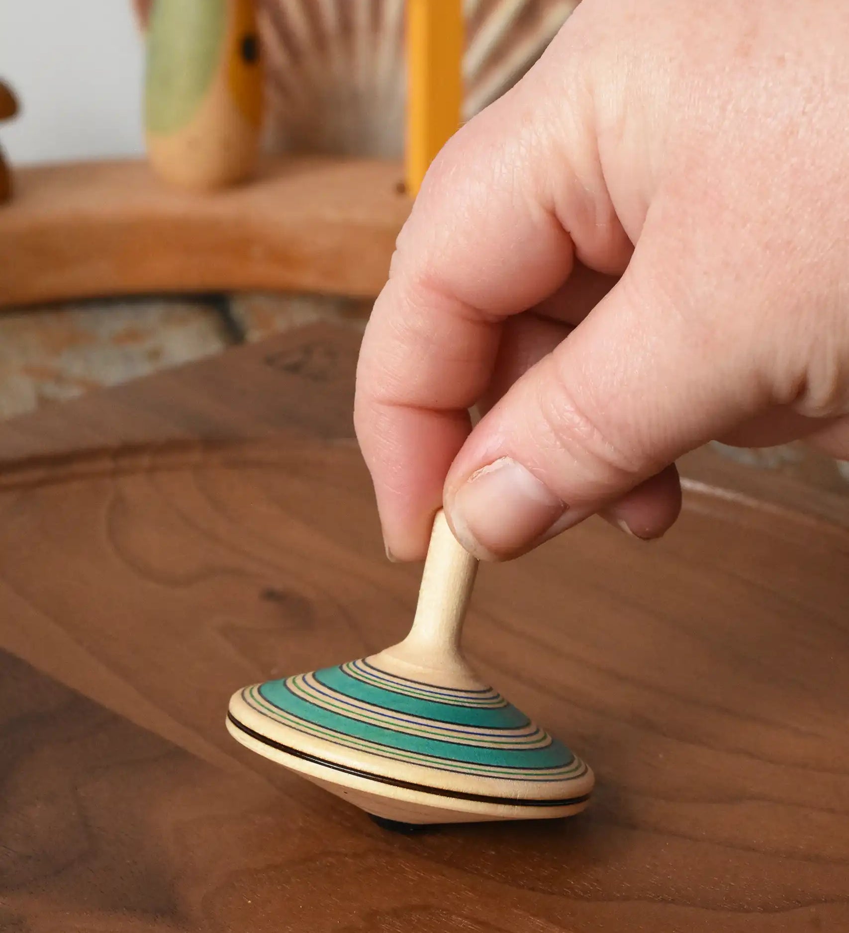 Mader Kreiselmanufaktur fado maple wooden finger spinning top being placed on a walnut spinning board by and adult hand in the Babipur playroom.
