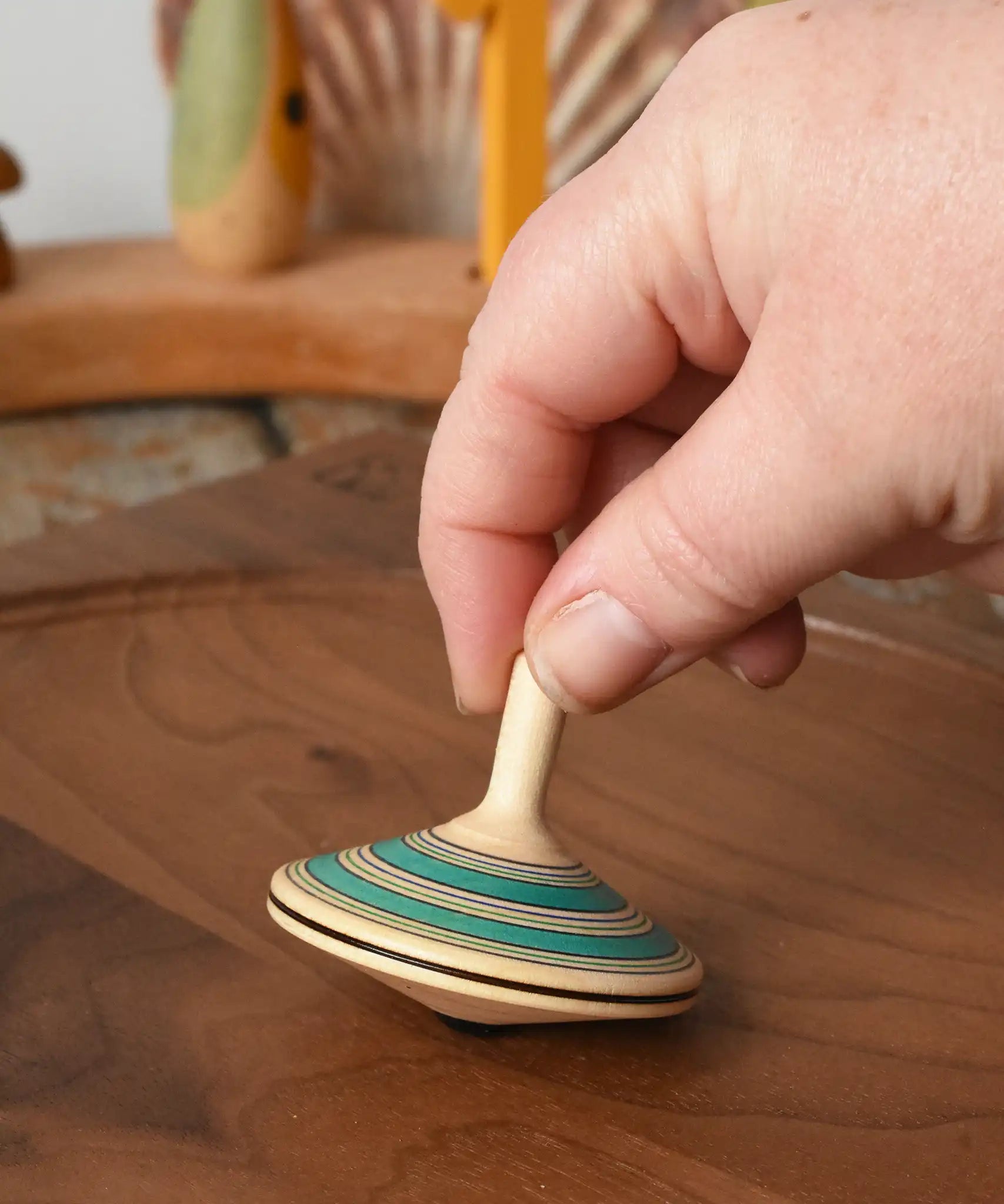Mader Kreiselmanufaktur fado maple wooden finger spinning top being placed on a walnut spinning board by and adult hand in the Babipur playroom.