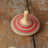 Red Mader Kreiselmanufaktur fado maple wooden finger spinning top placed on a wooden surface in the Babipur playroom.