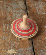 Red Mader Kreiselmanufaktur fado maple wooden finger spinning top placed on a wooden surface in the Babipur playroom.