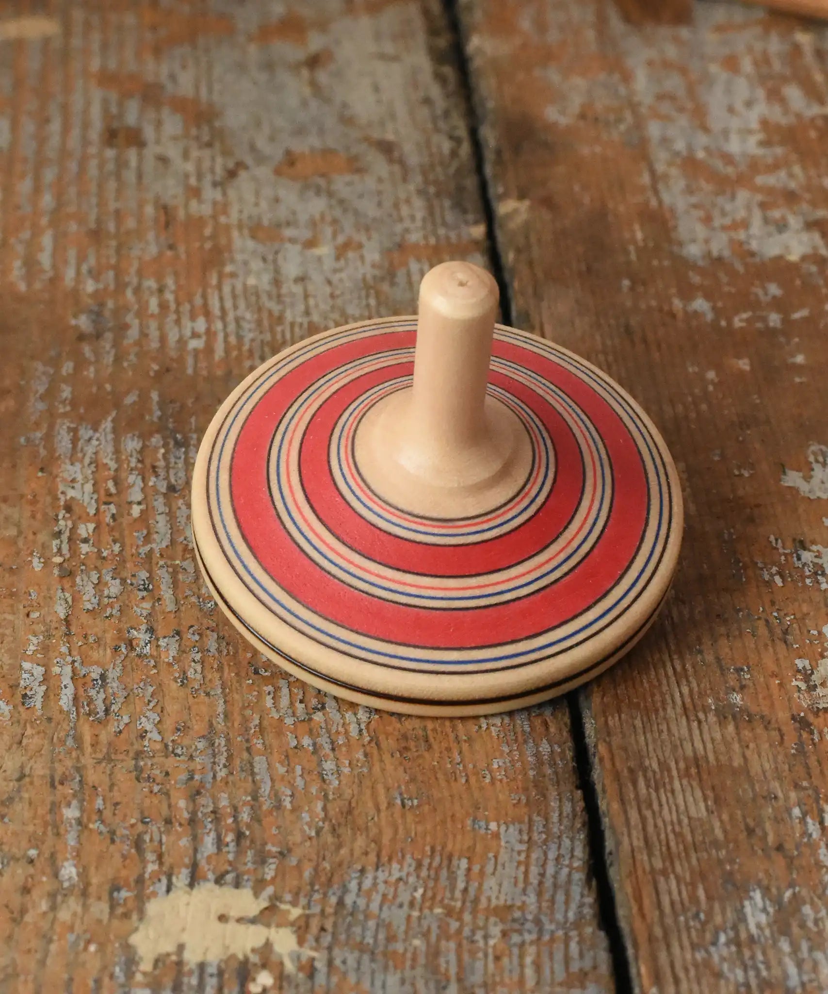 Red Mader Kreiselmanufaktur fado maple wooden finger spinning top placed on a wooden surface in the Babipur playroom.
