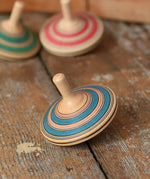 Mader Kreiselmanufaktur fado maple wooden finger spinning top placed on a wooden surface in the Babipur playroom. Other colour variants can be seen in the background. 