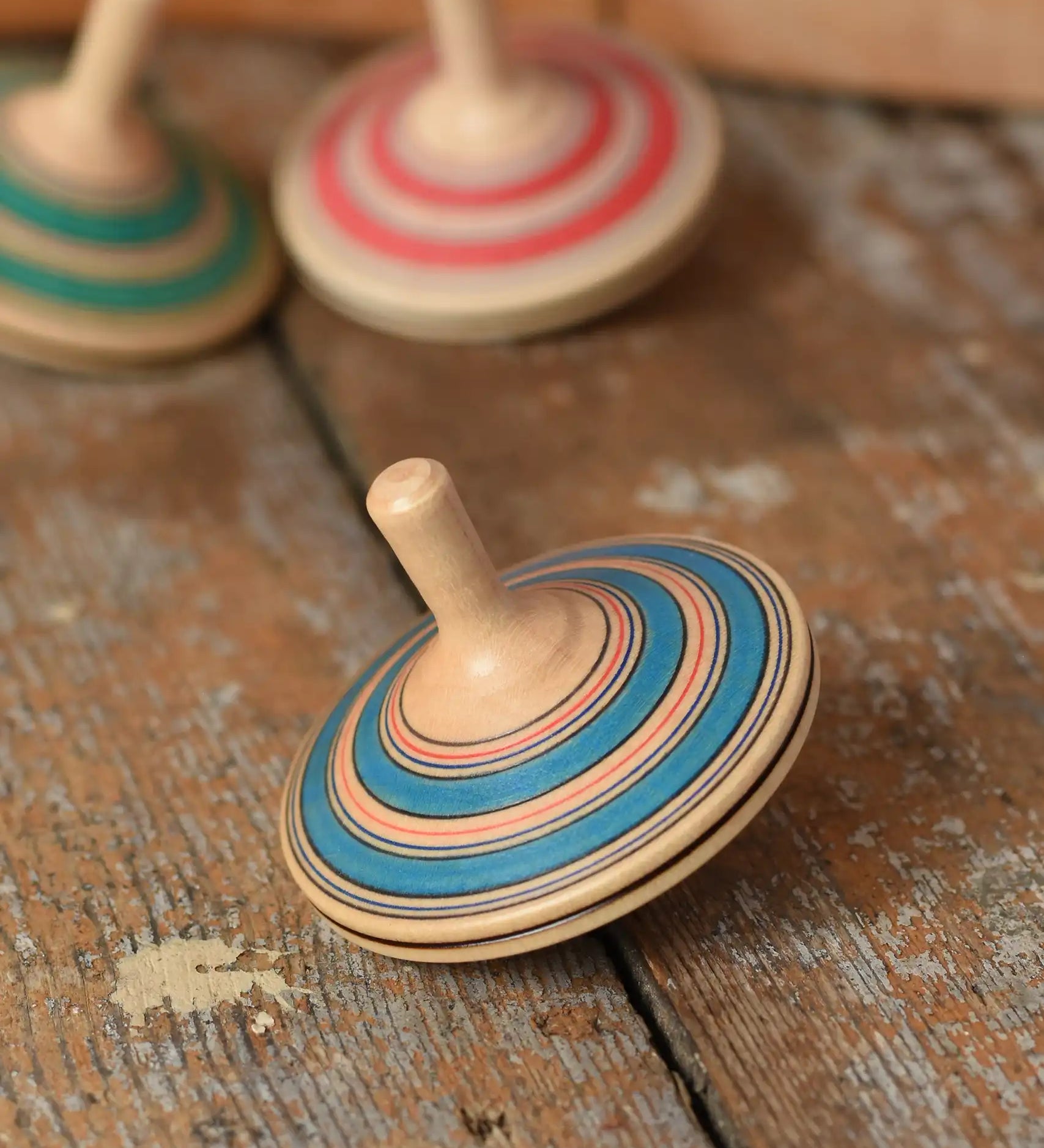 Mader Kreiselmanufaktur fado maple wooden finger spinning top placed on a wooden surface in the Babipur playroom. Other colour variants can be seen in the background. 