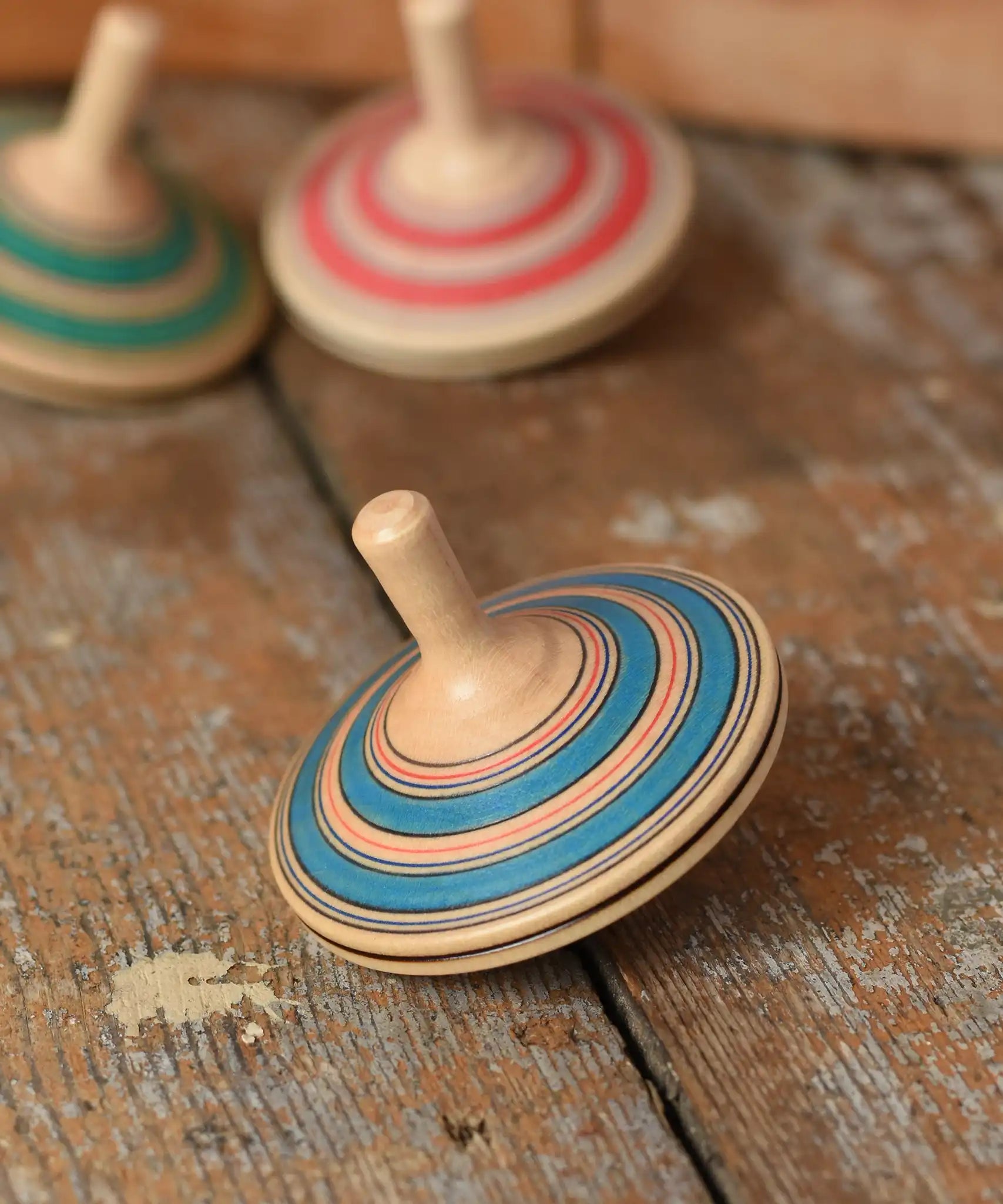 Mader Kreiselmanufaktur fado maple wooden finger spinning top placed on a wooden surface in the Babipur playroom. Other colour variants can be seen in the background. 