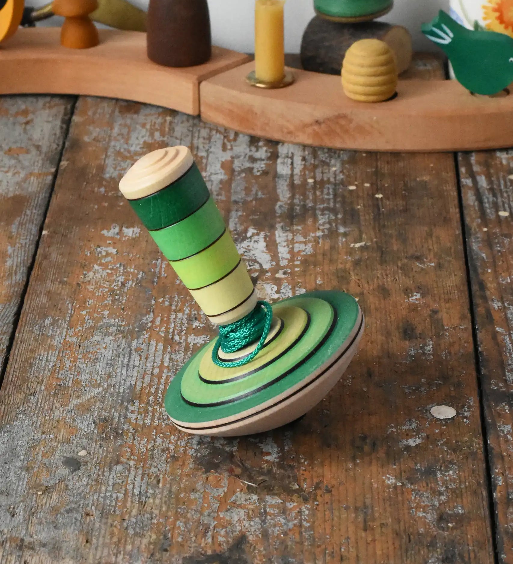 Mader wooden my first spinning top toy with starter in green placed on a wooden surface in the Babipur playroom.