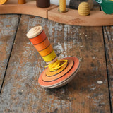 Mader wooden my first spinning top toy with starter in orange placed on a wooden surface in the Babipur playroom.
