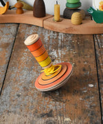 Mader wooden my first spinning top toy with starter in orange placed on a wooden surface in the Babipur playroom.
