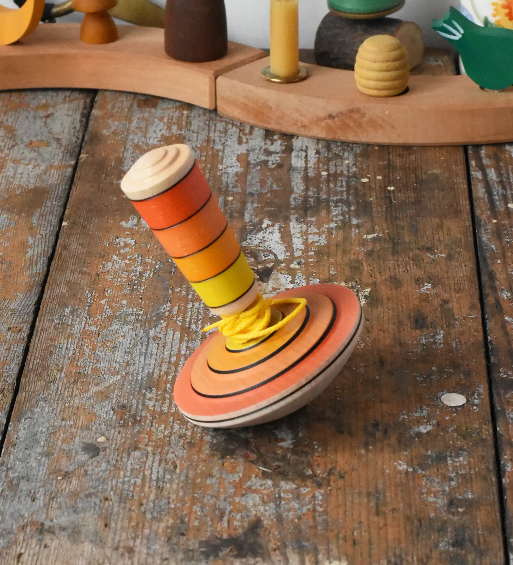 Mader wooden my first spinning top toy with starter in orange placed on a wooden surface in the Babipur playroom.