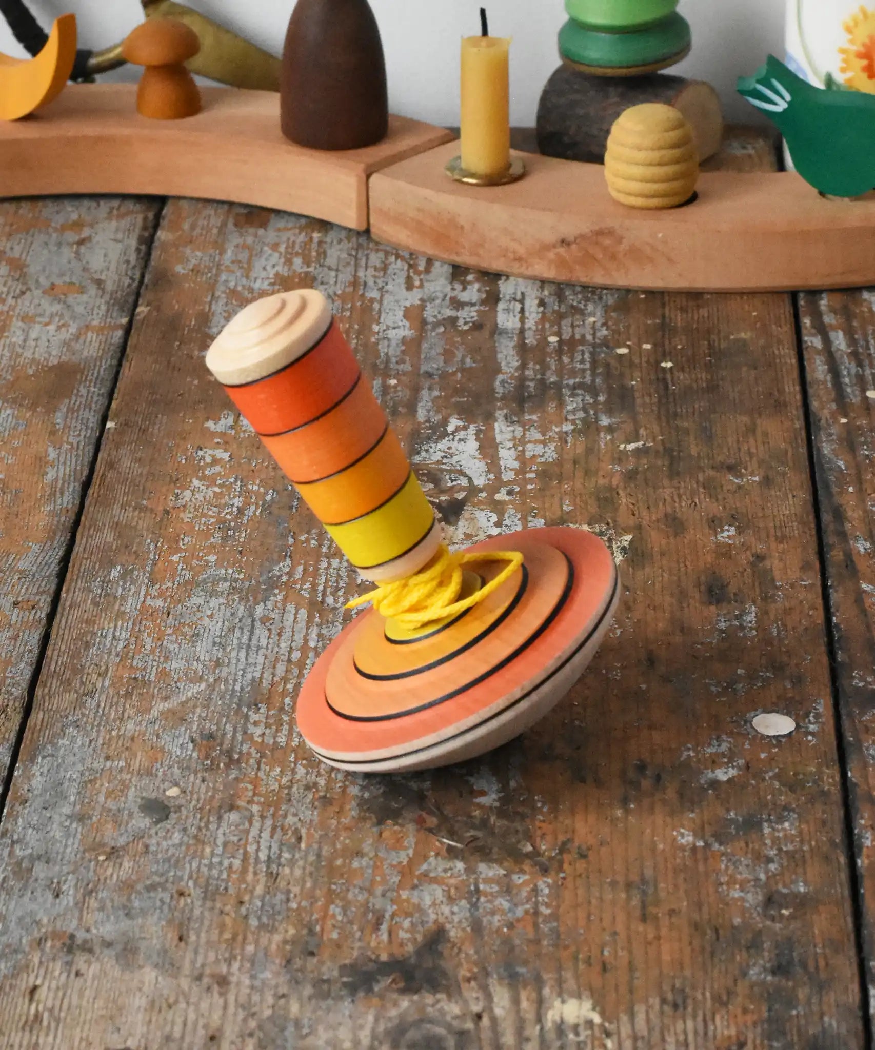Mader wooden my first spinning top toy with starter in orange placed on a wooden surface in the Babipur playroom.