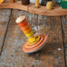 Mader wooden my first spinning top toy with starter in orange placed on a wooden surface in the Babipur playroom.