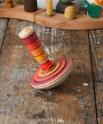 Mader wooden my first spinning top toy with starter in red placed on a wooden surface in the Babipur playroom.